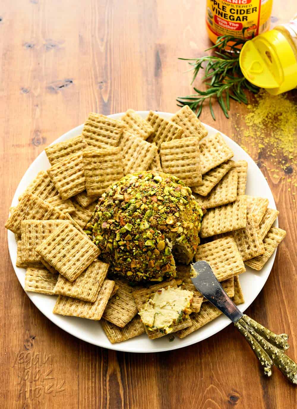 Picture of pistachio-rosemary cheese ball on a plate surrounded by crackers