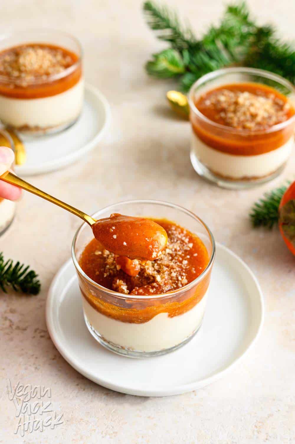 Persimmon cheesecake in a glass, on a white saucer with gold spoon scooping it out