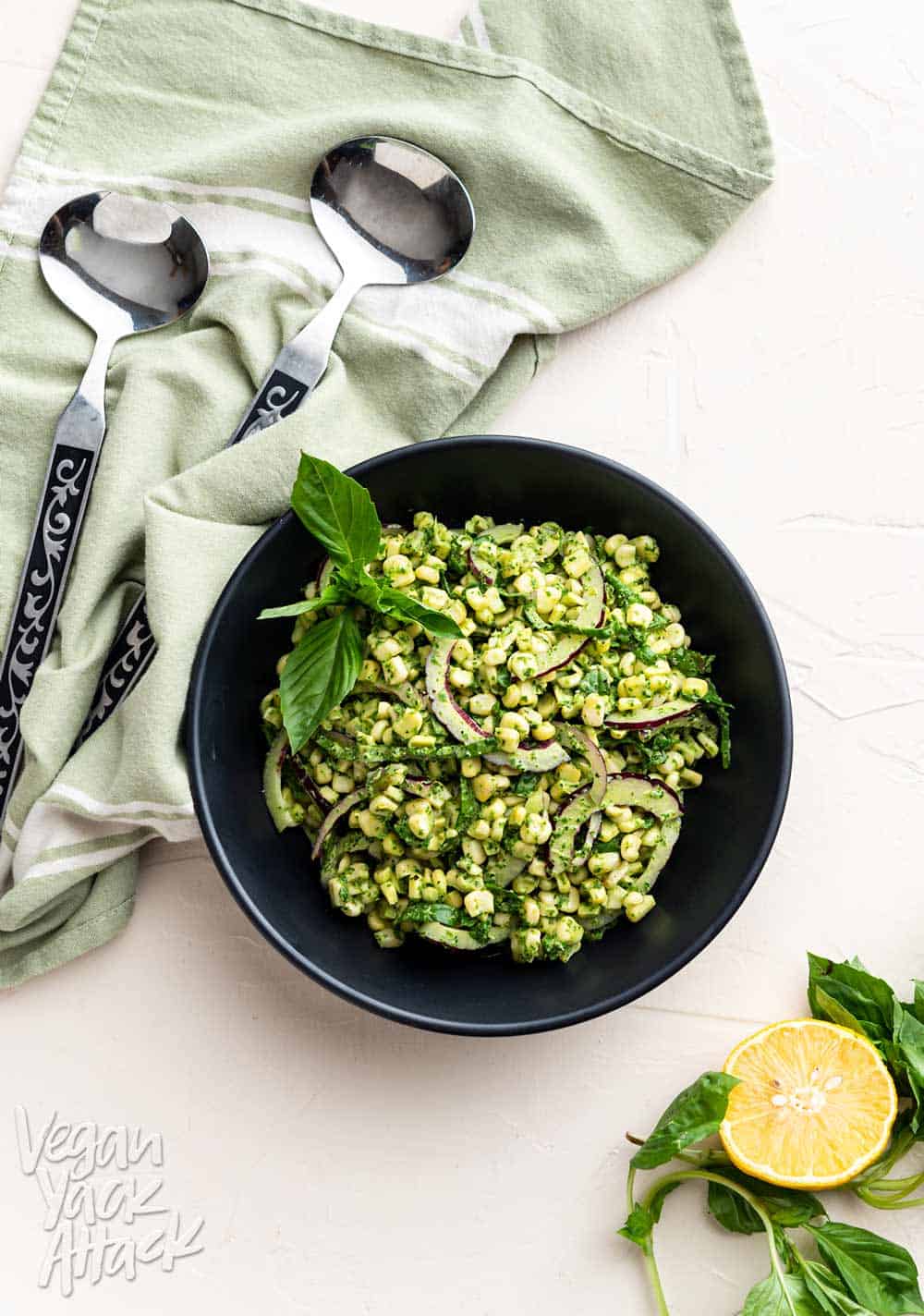 Large black bowl filled with Summer corn salad and basil pesto aioli with tongs and linen nearby