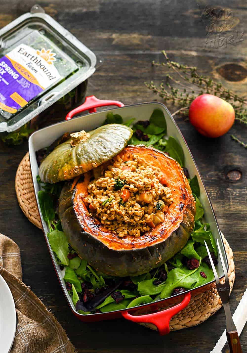 A large, roasted kabocha squash centerpiece, in a casserole dish, stuffed with a rice/tempeh mixture, on a dark background.
