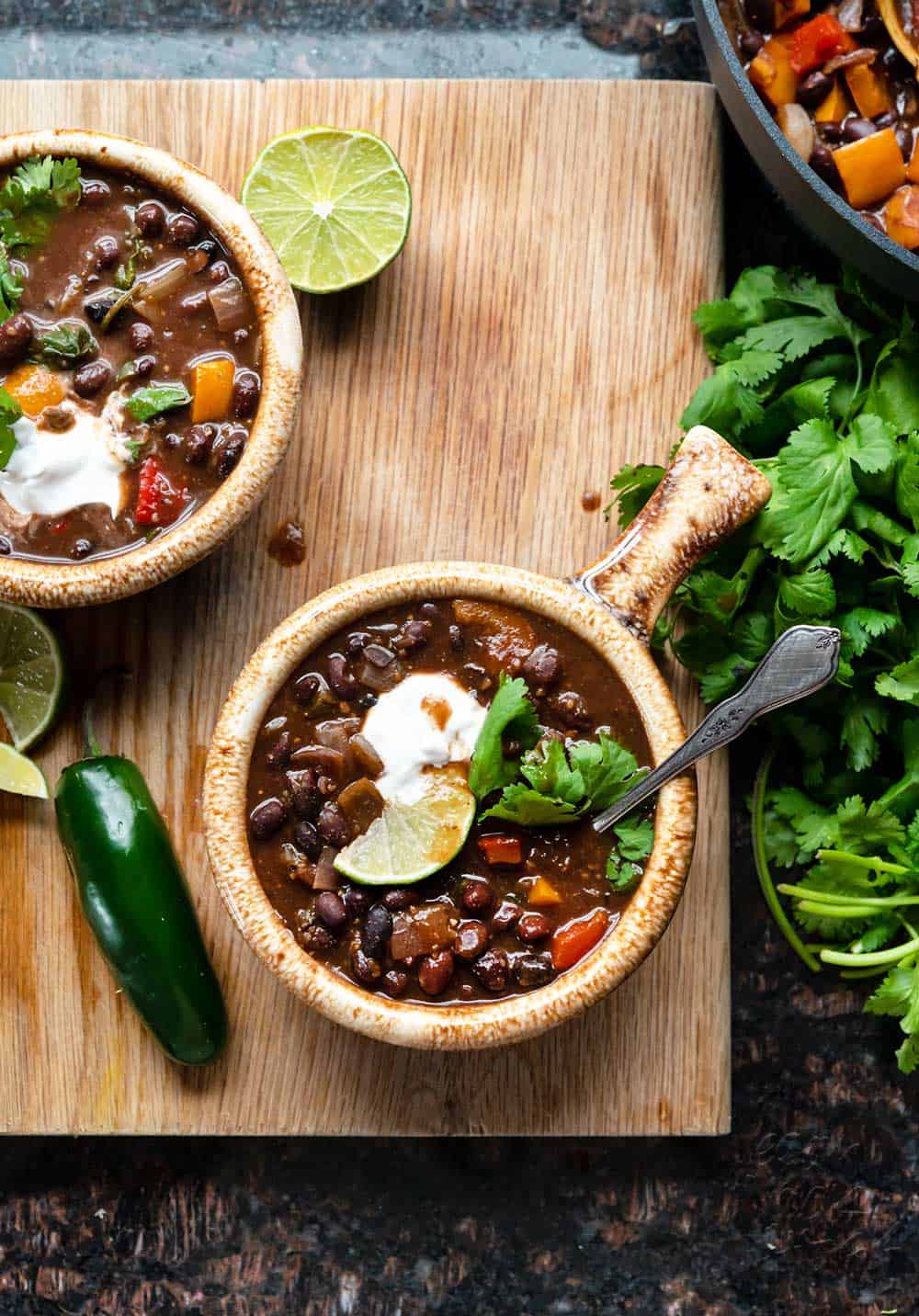 Image of two bowls of black bean stew on a cutting board with fresh cilantro bundle
