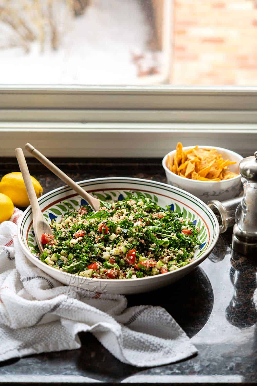 Image of kale quinoa tabbouleh salad in a large ceramic bowl, on granite countertop.