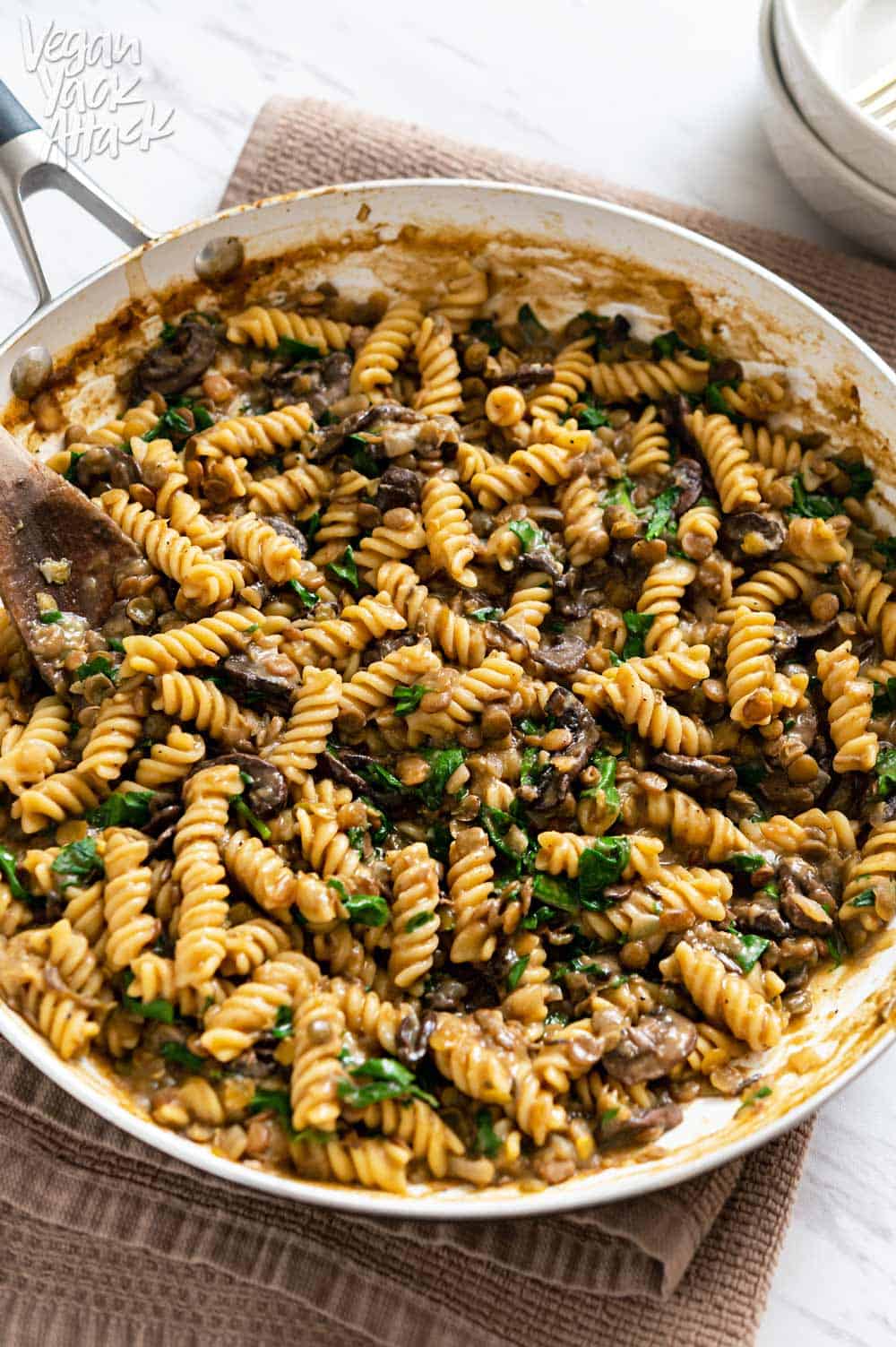 Image of a close-up of one-pot lentil mushroom pasta in a large pan sitting on a towel