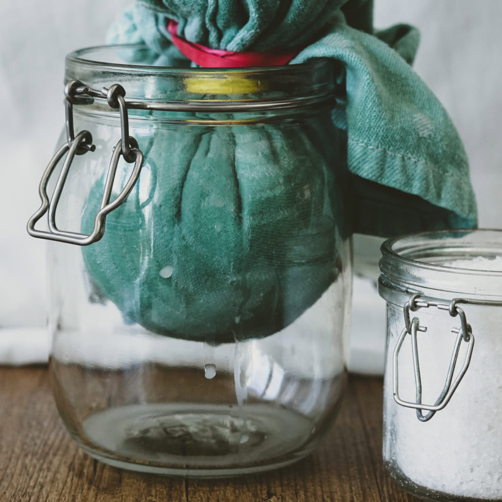 Ein Tuch voller Joghurt in einem Einmachglas, grobes Salz daneben