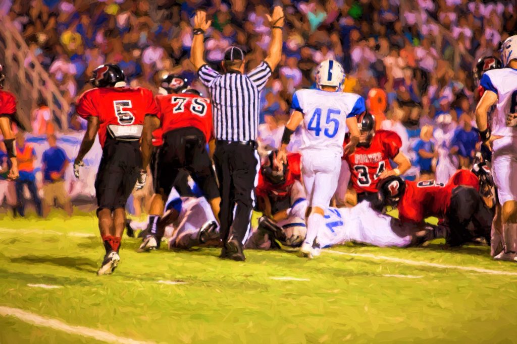 Referee calling a touchdown at a high school football game with players on the field.