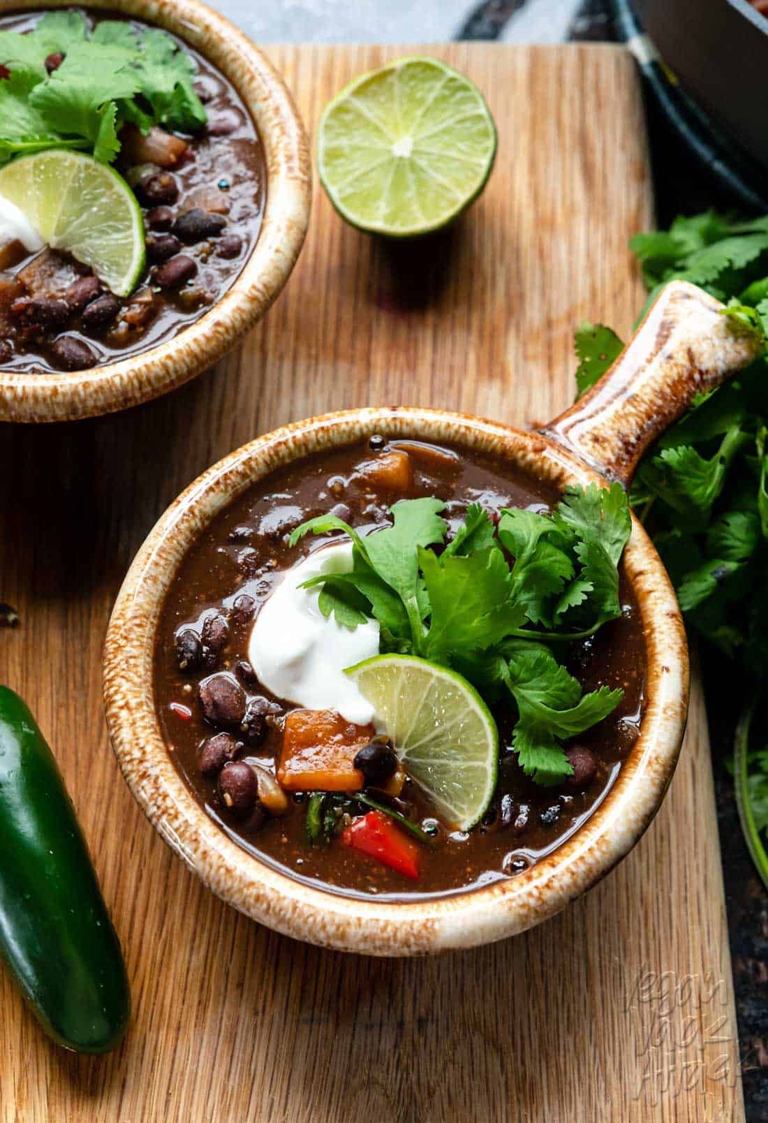 Image of two bowls of black bean stew on a cutting board with fresh cilantro bundle