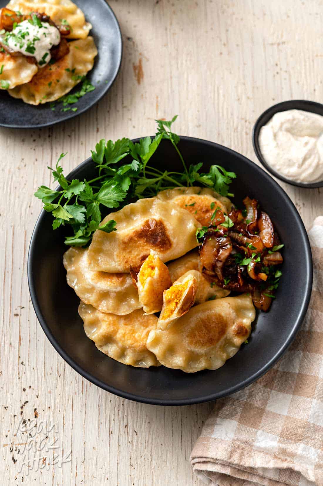 Image of black bowl filled with cheesy sweet potato pierogi, on a white table