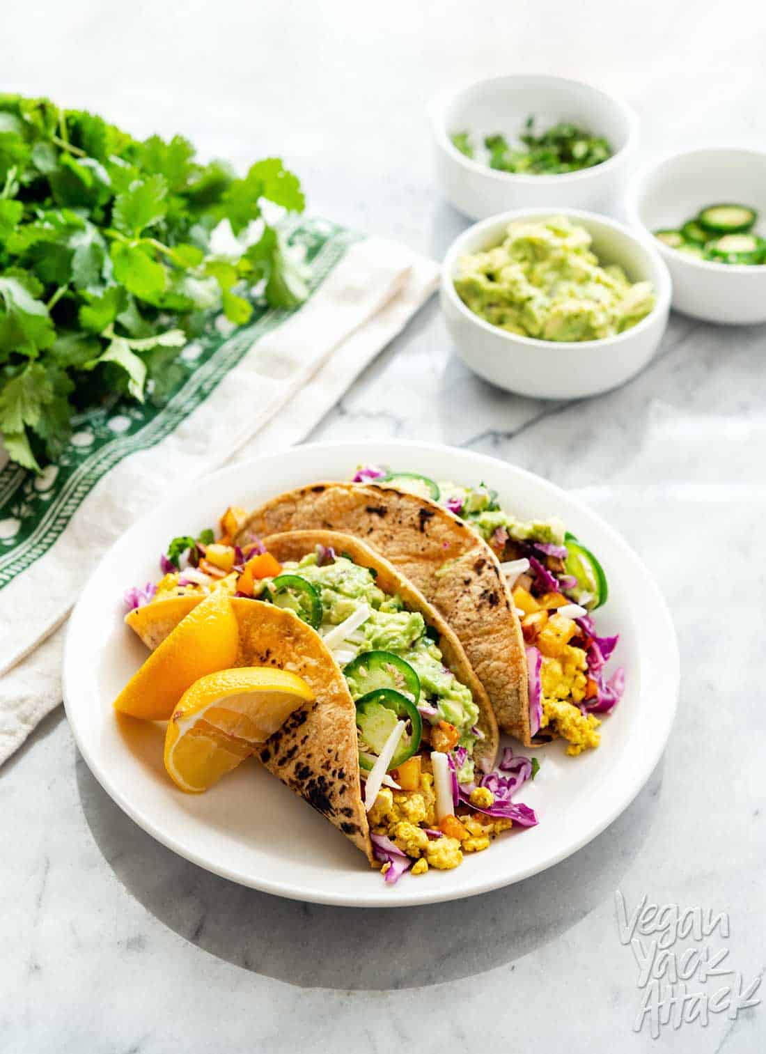 An image of vegan breakfast tacos plated, on a marble table with assorted toppings near it
