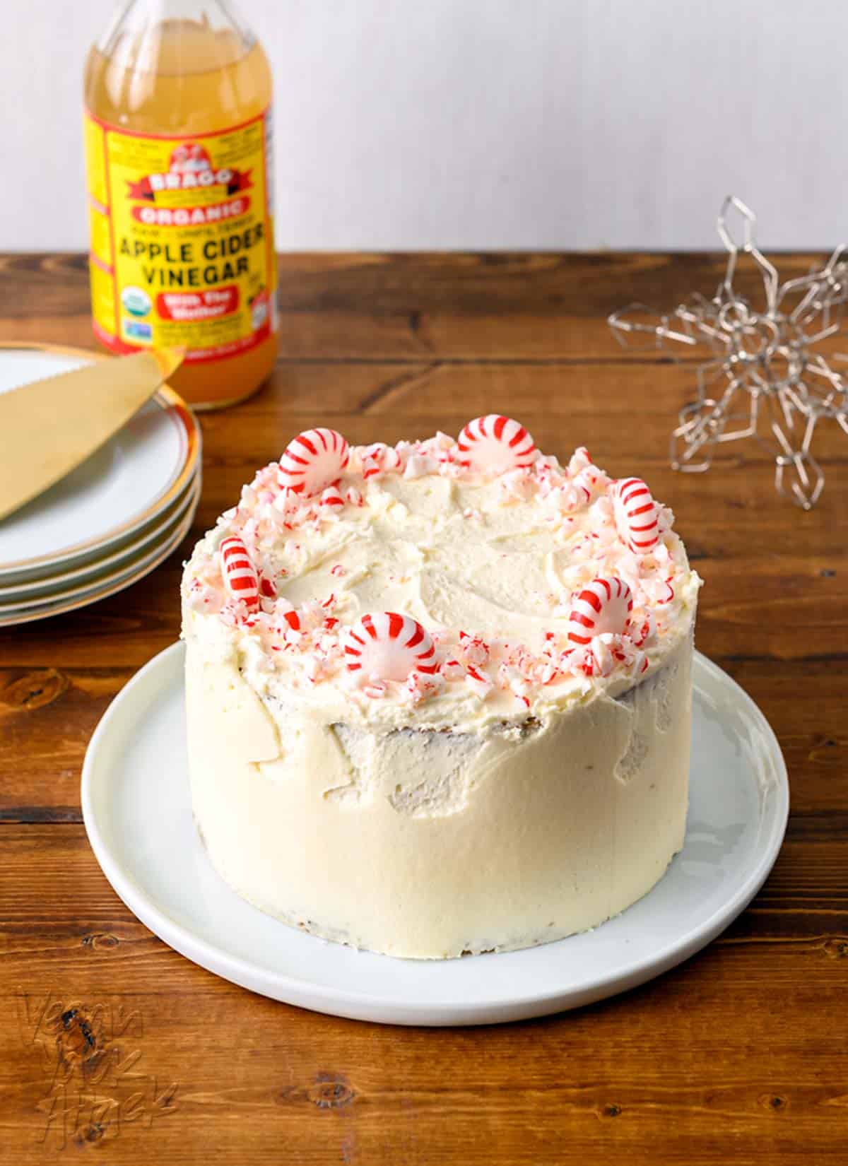 Image of small, layered cake with peppermints on top, serving plates and apple cider vinegar beside it.