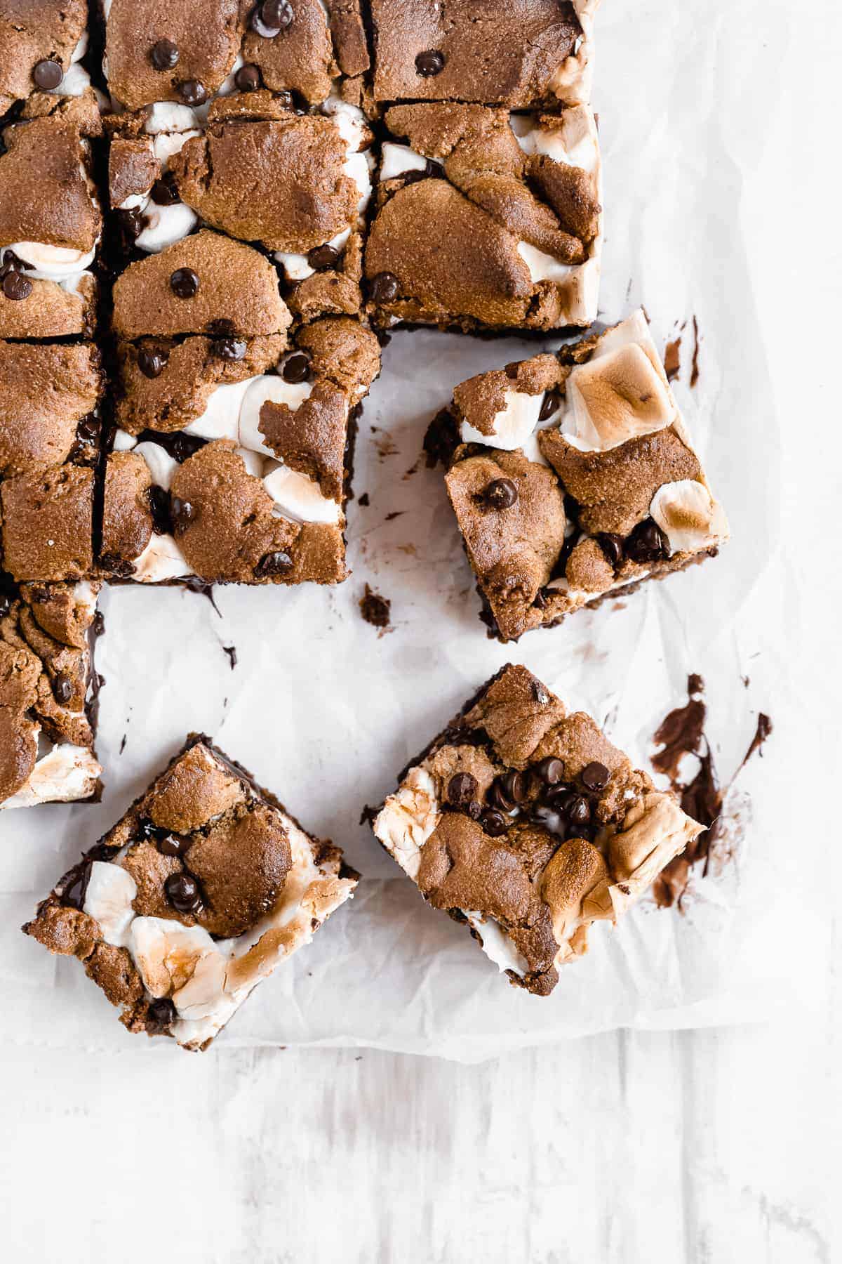 Three s'mores bars scattered on a white sheet with chocolate.