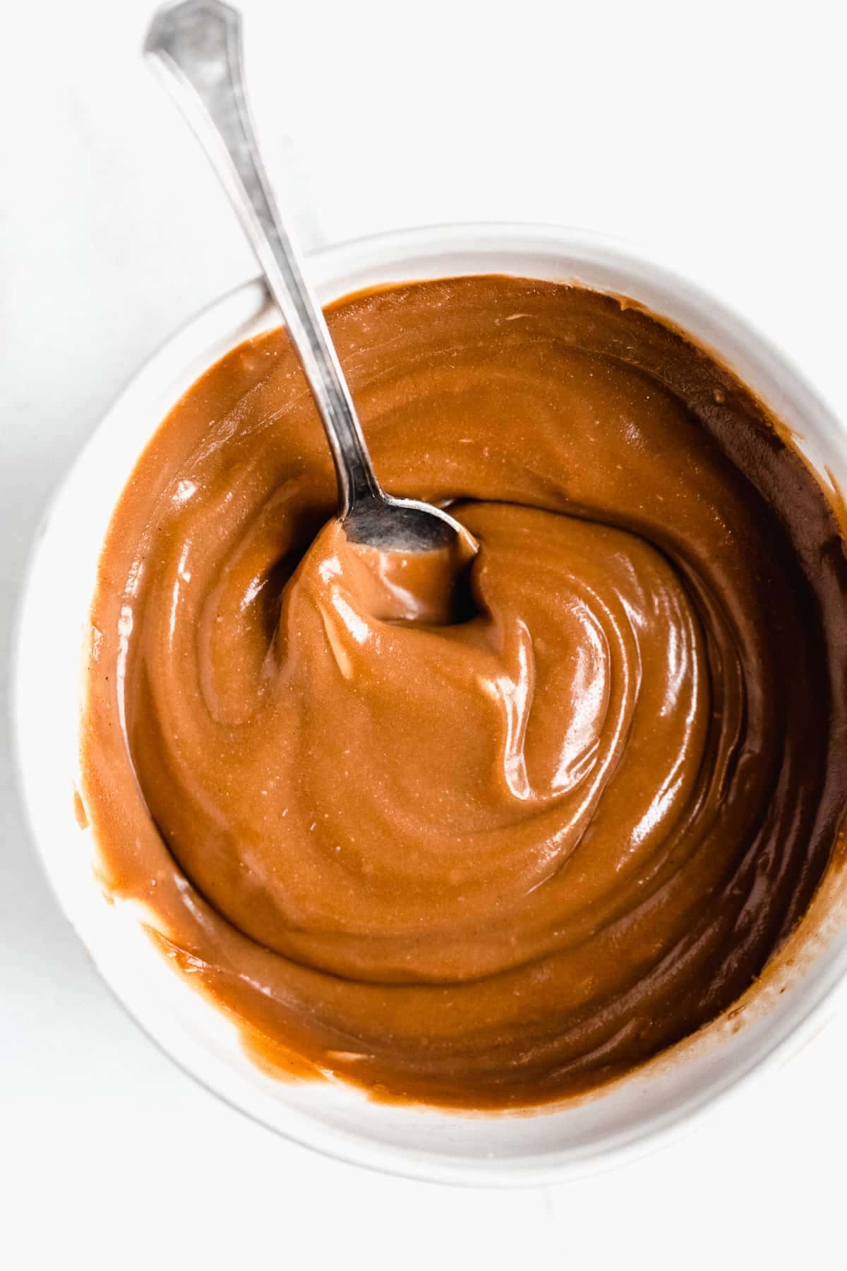 Overhead closeup photo of the 3-Ingredient Vegan Caramel Sauce in a small jar and a spoon sticking up in the middle of the jar.