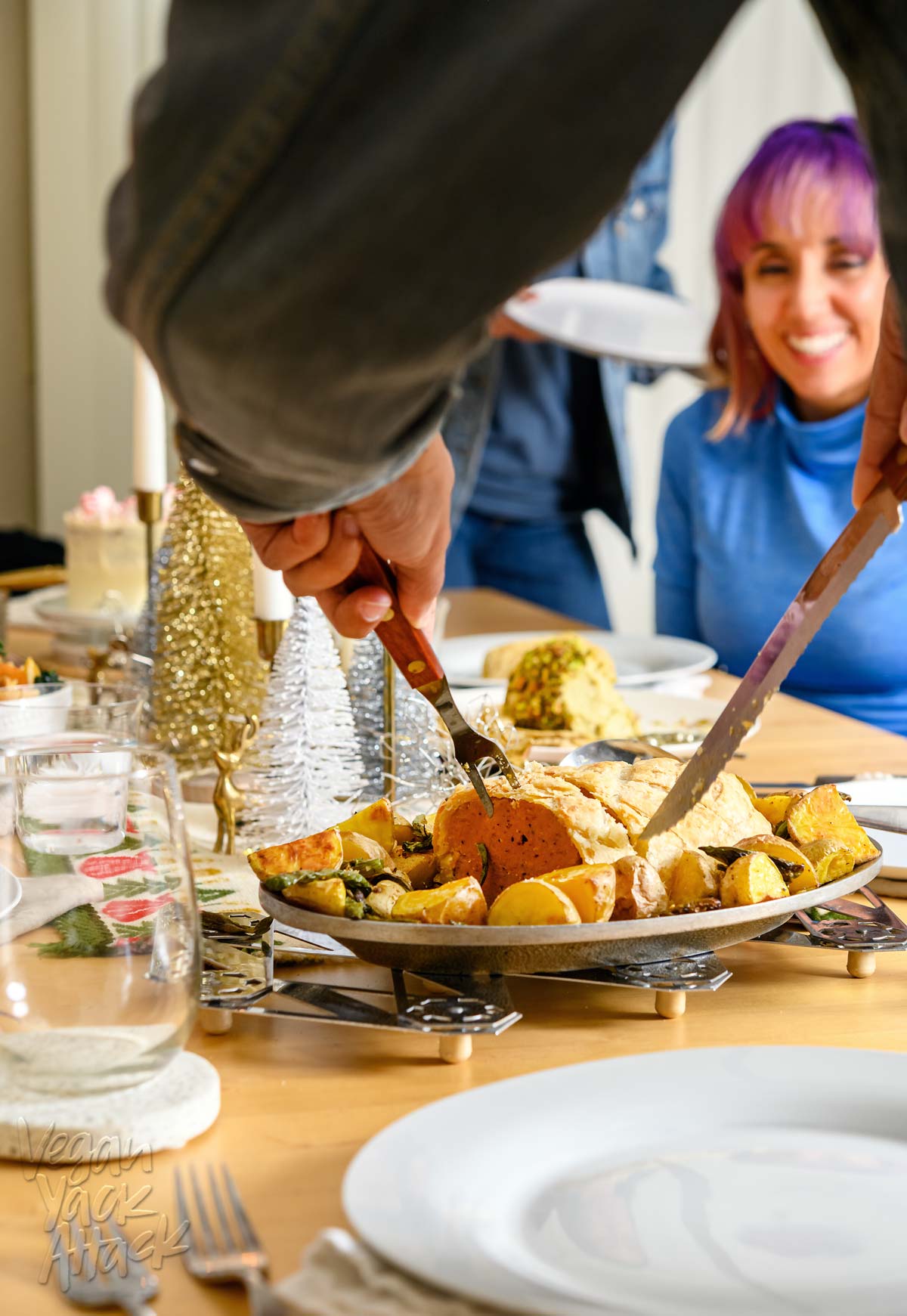 An image of an adult cutting into a seitan Wellington in a holiday dinner table setting