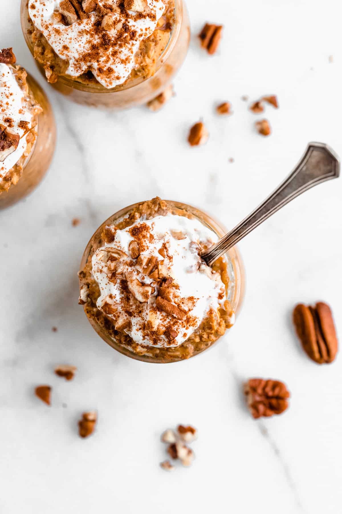 Overhead shot of a jar of pumpkin spice overnight oats with a dollop of yogurt on top, chopped pecans, and cinnamon.