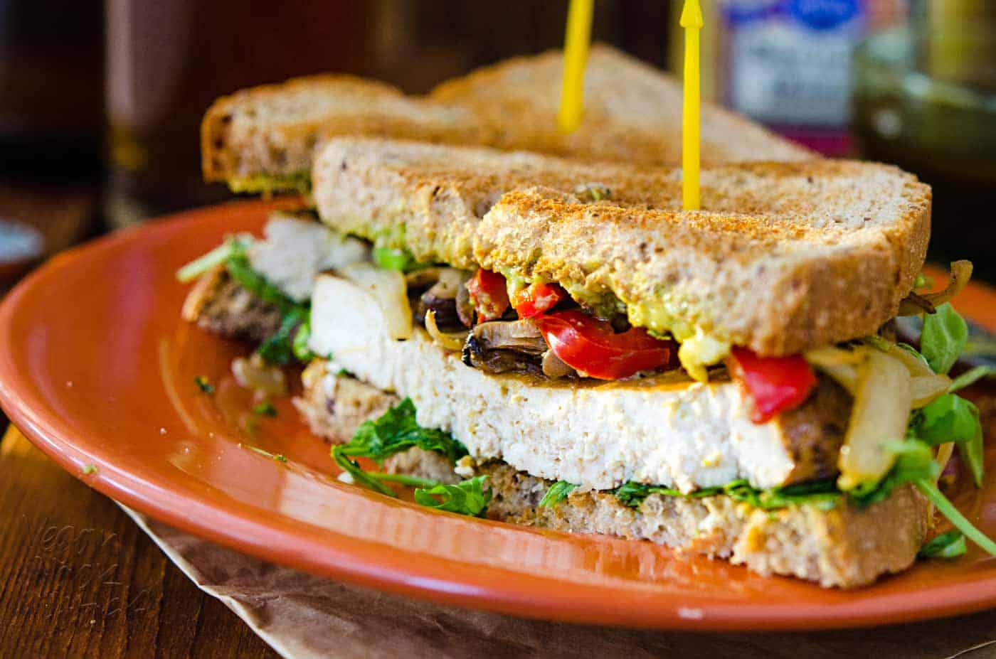 Balsamic Baked Tofu Sandwich on an orange plate, with beer in the background