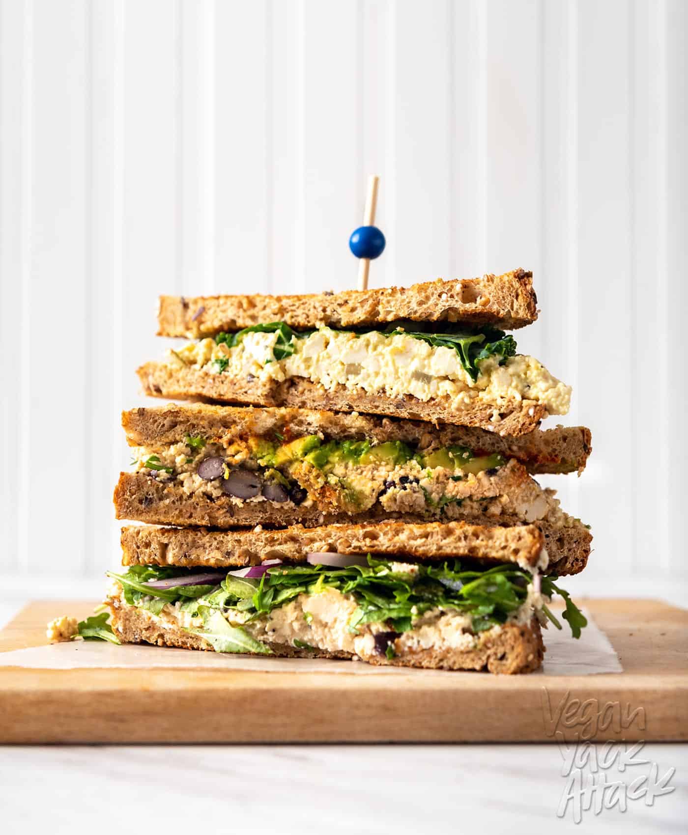 Image of three tofu 'egg' salad sandwiches stacked on one another on a cutting board