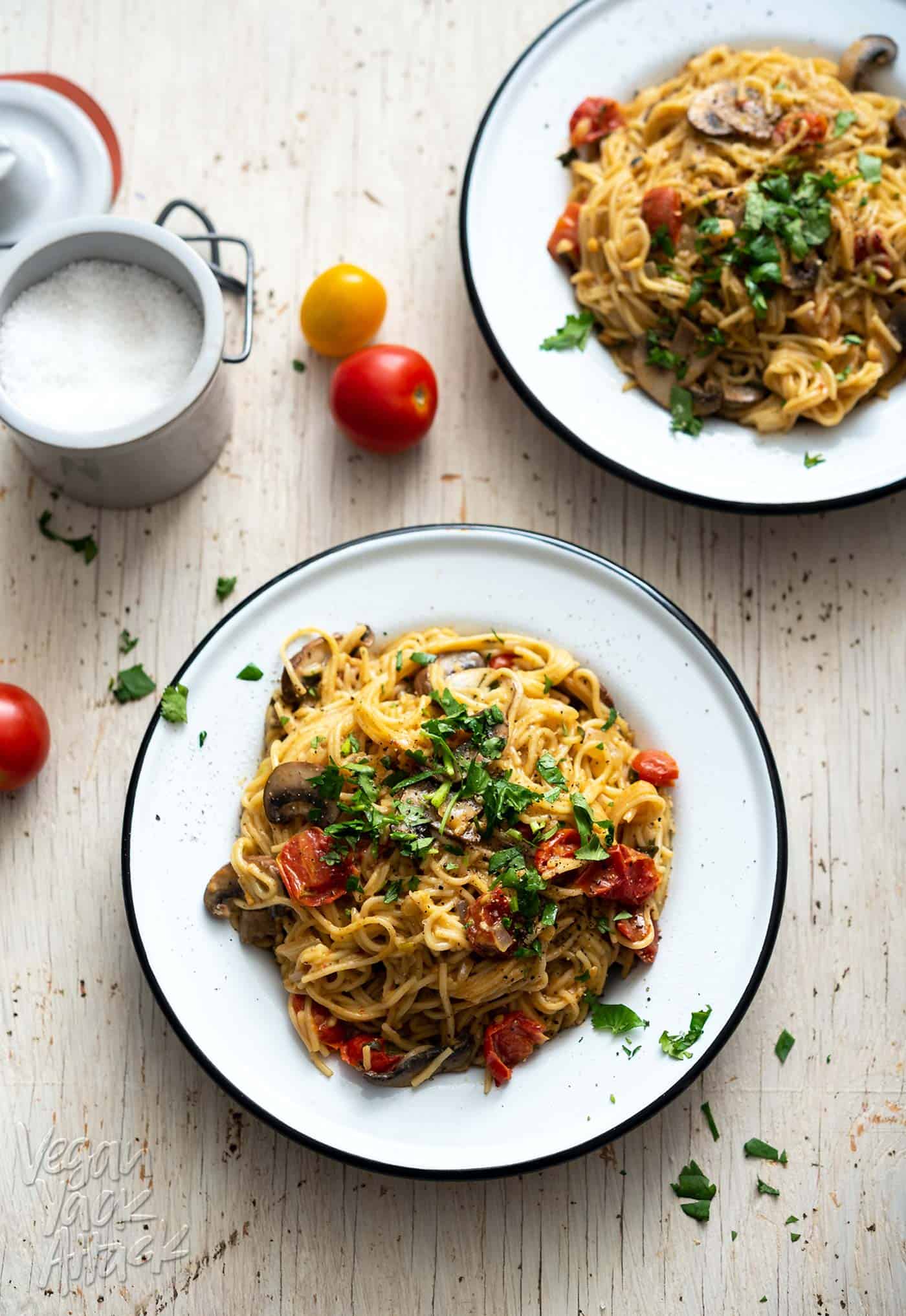 Image of two bowls of pasta on a white wood table top, with salt on the side