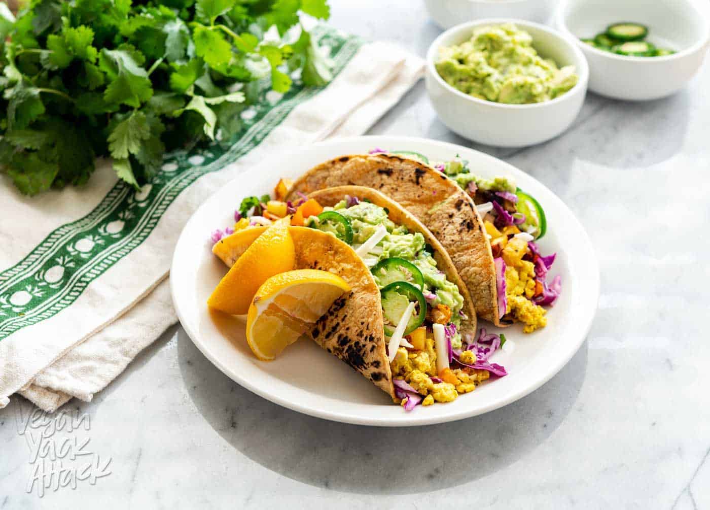 An image of vegan breakfast tacos plated, on a marble table with assorted toppings near it