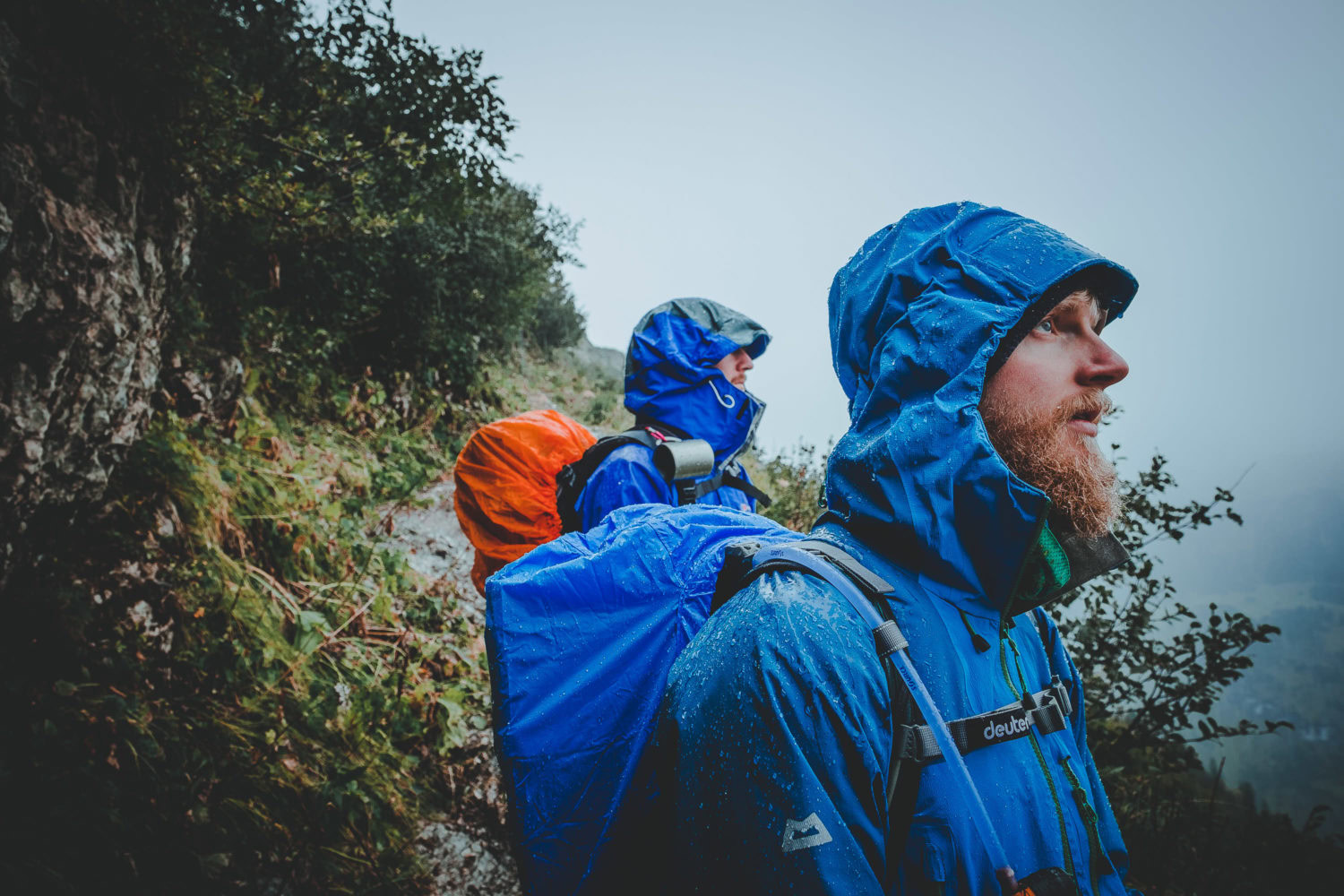 Zwei Perspnen stehen im Regen mit blauen Regenjacken