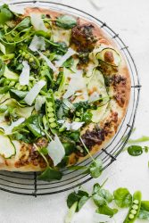 A homemade Spring Green Pizza made with pesto, zucchini, spring peas, watercress, mozzarella, and a green goddess dressing.