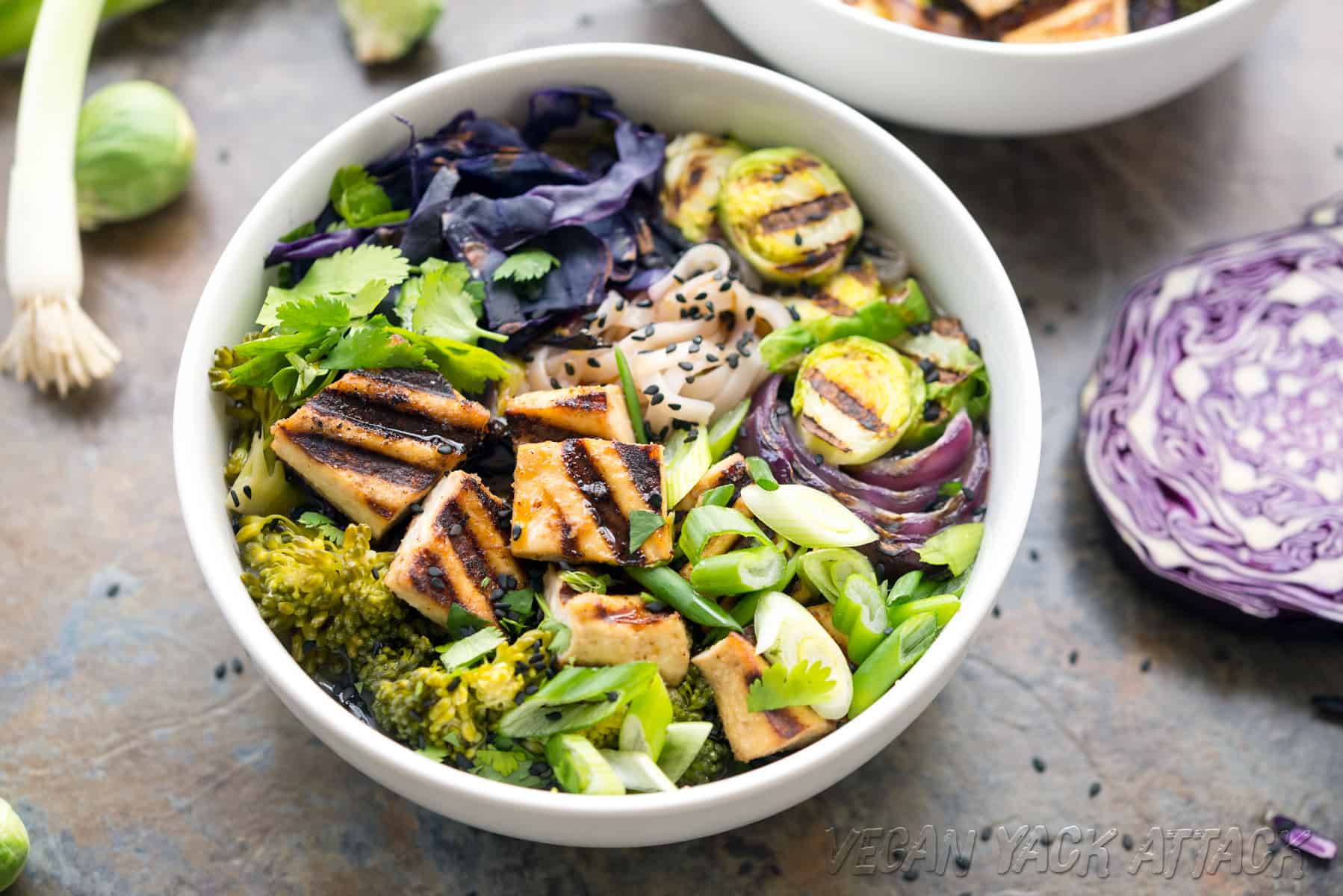 Image of bowl of soup topped with grilled tofu and veggies on a gray background