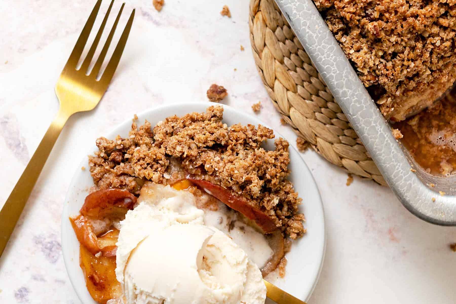 A small plate with a scoop of ice cream and scoop of apple pear crisp with gold forks