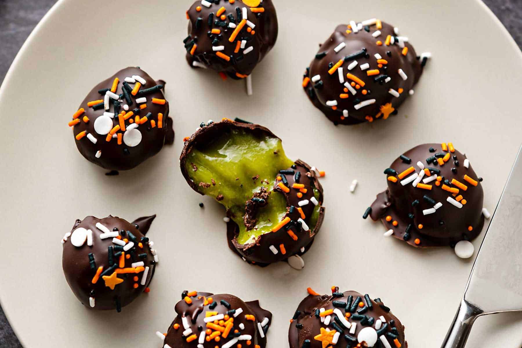 Small light grey plate of truffles with green filling on a black marble background