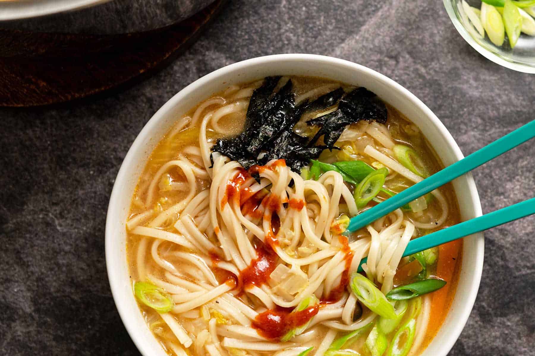 Udon noodle soup in a large white bowl with teal chopsticks
