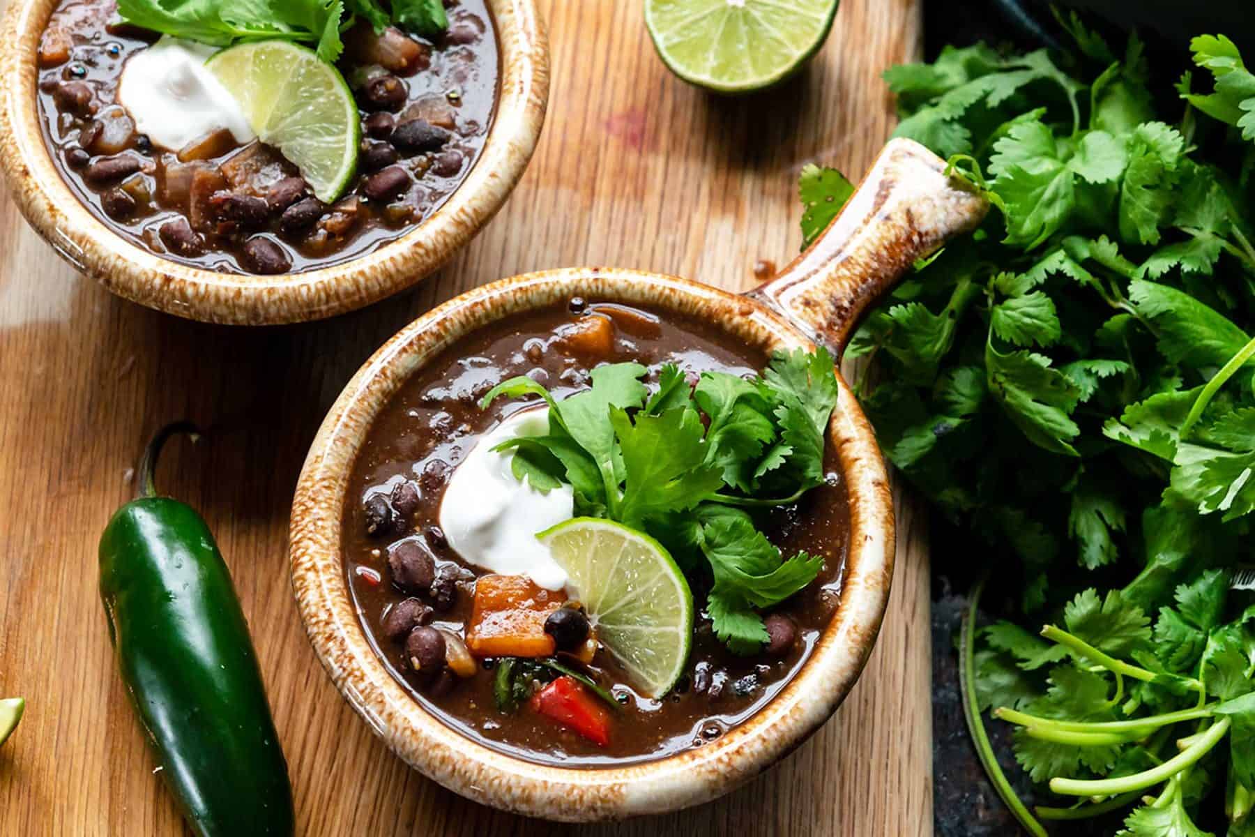 Image of two bowls of black bean stew on a cutting board with fresh cilantro bundle
