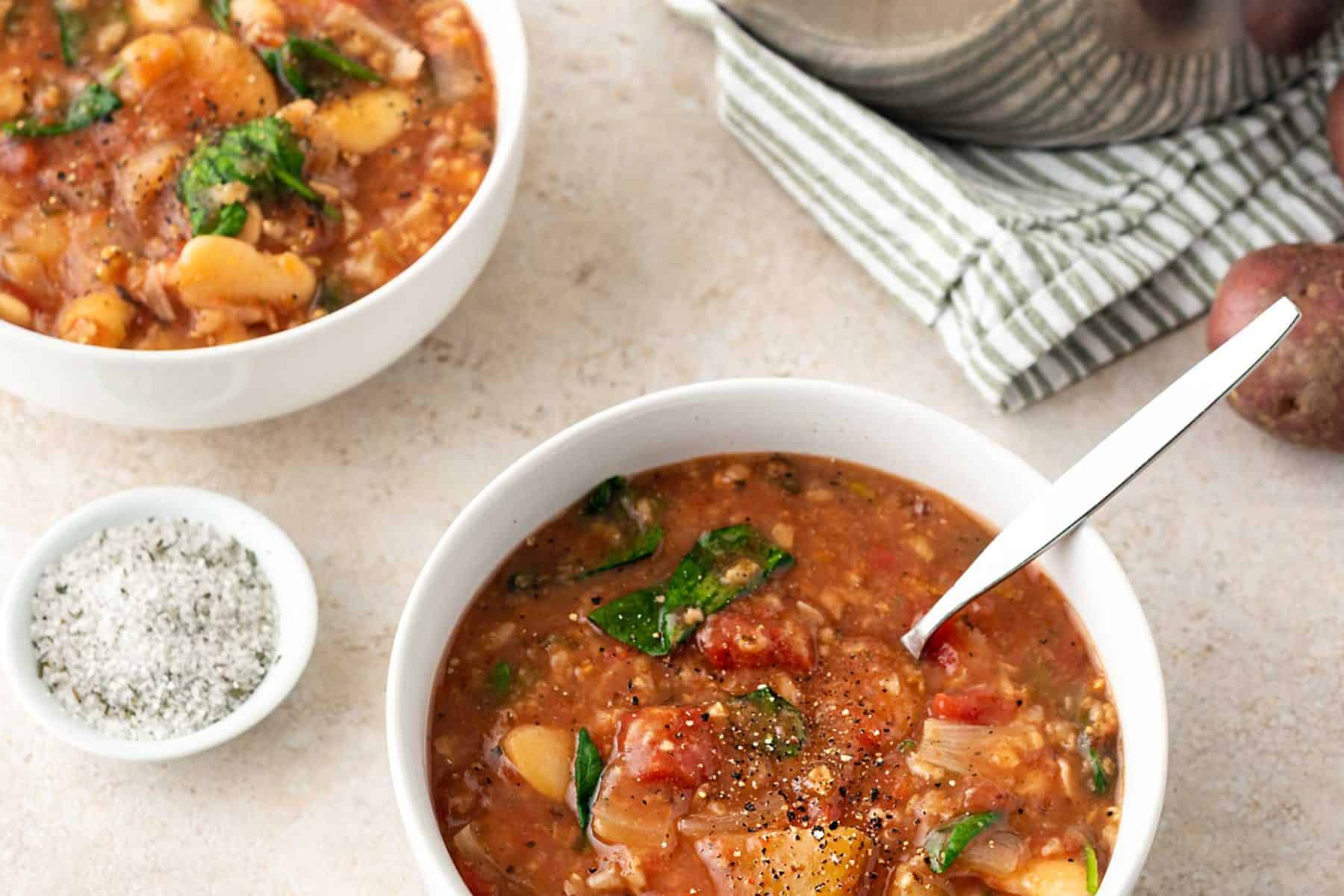 A picture of two bowls of slow cooker lima bean tomato stew, next to an Instant Pot insert, on a light table top