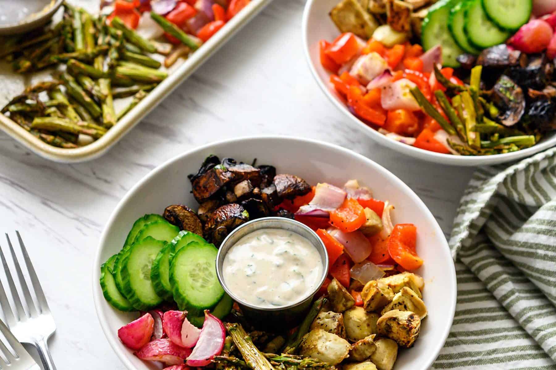 Image of two bowls, filled with a Mediterranean Sheet Pan Meal, and sauce, next to a sheet pan, with text overlay