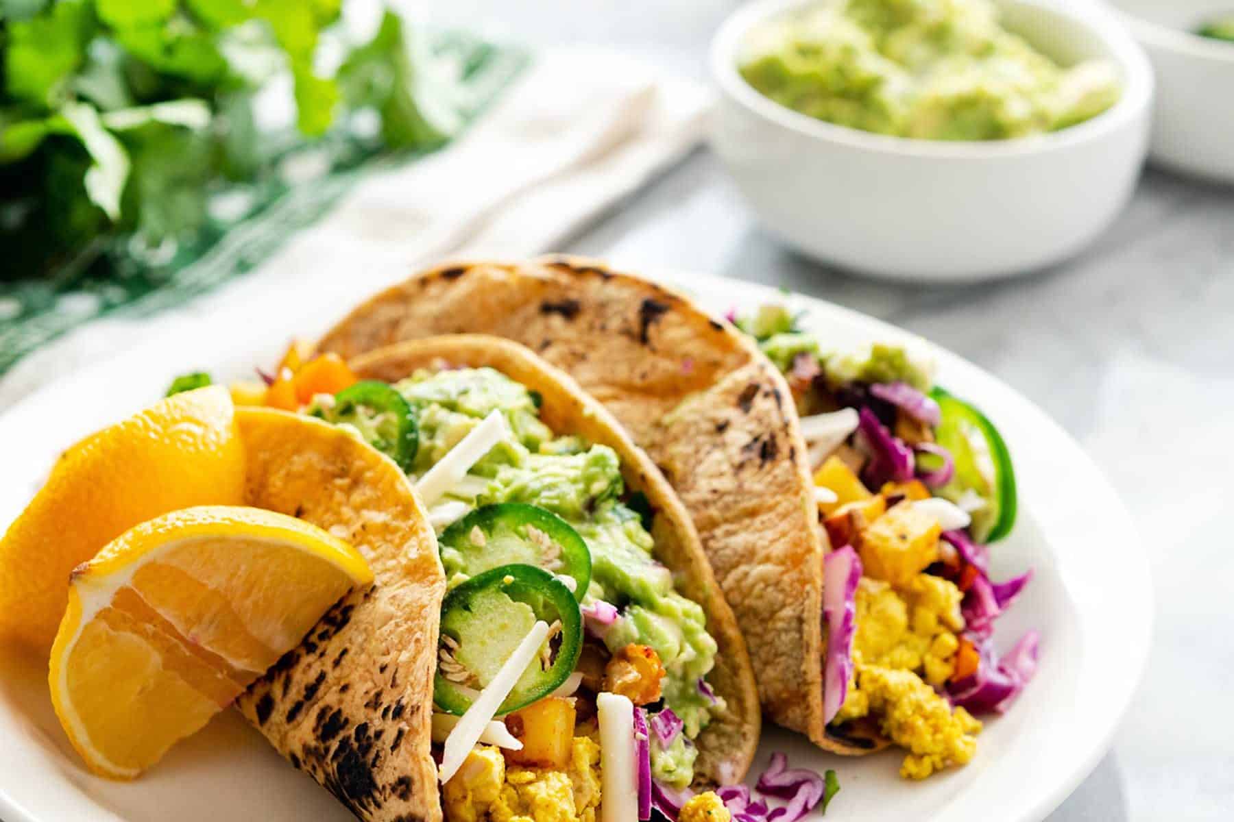 An image of vegan breakfast tacos plated, on a marble table with assorted toppings near it