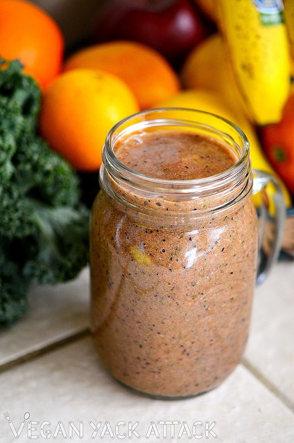 Speckled Strawberry Smoothie in a glass jar in front of fresh fruit and kale