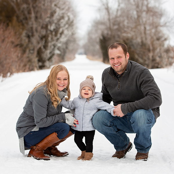 Kidrowski_Creative_family_photography_sessions A young couple with their toddler kneeling on a snow covered path.