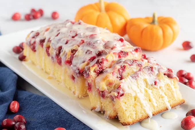 Orange Cranberry Bread on a white platter next to baby pumpkins and fresh cranberries.