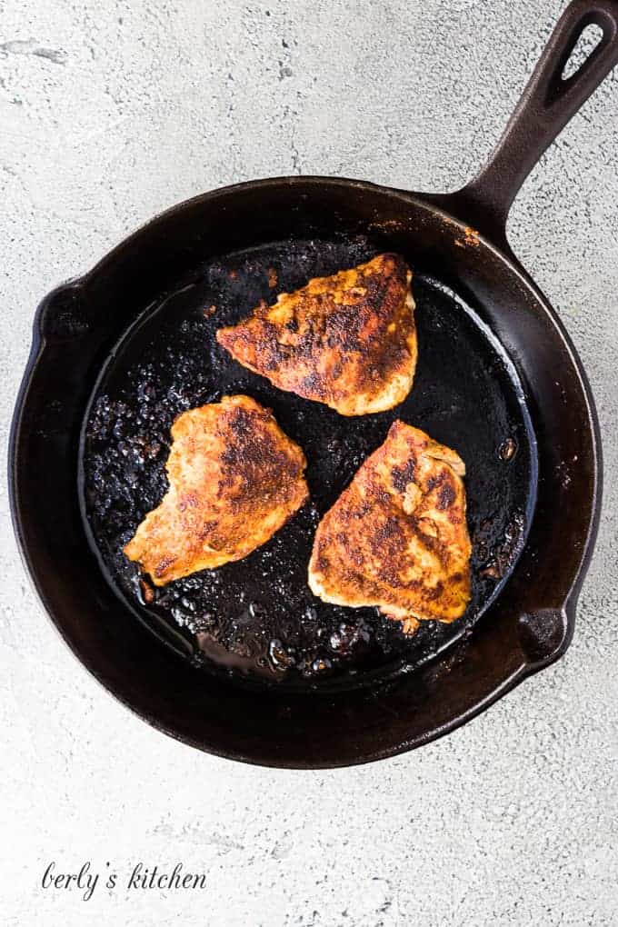 Three seasoned chicken breasts cooking in a cast iron skillet.