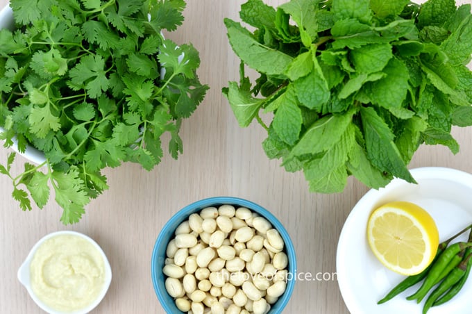 coriander leaves, mint leaves, peanuts, slice of lemon, few green chilies and some garlic paste set on a table.
