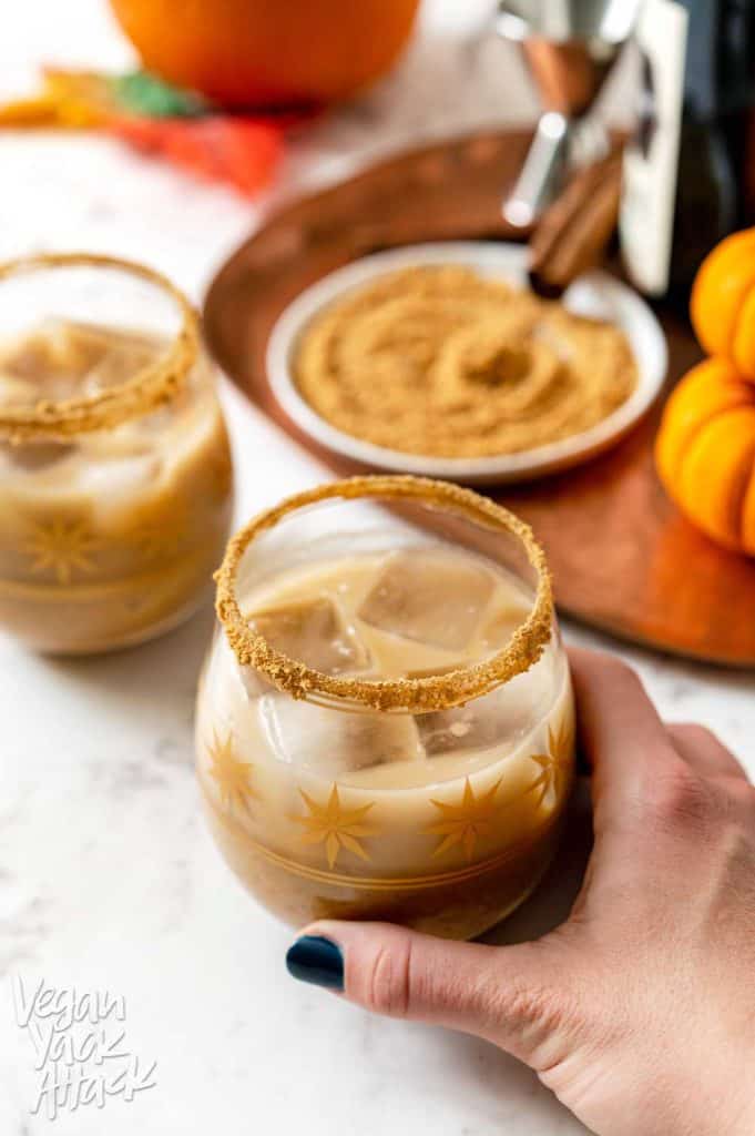 Two glasses filled with a tan-colored cocktail and pumpkins around them