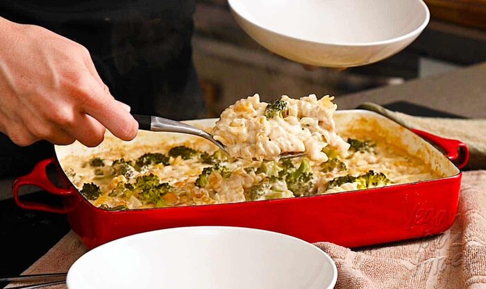 Hand using spoon to scoop pasta casserole into a bowl