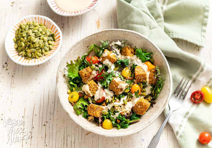 Comforting Tempeh Kale Salad in a ceramic bowl next to a green linen and fork