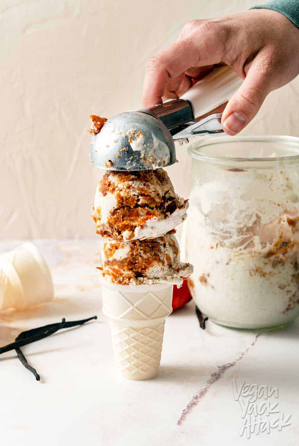 Two scoops of persimmon vanilla ice cream being placed on a cone, next to a persimmon