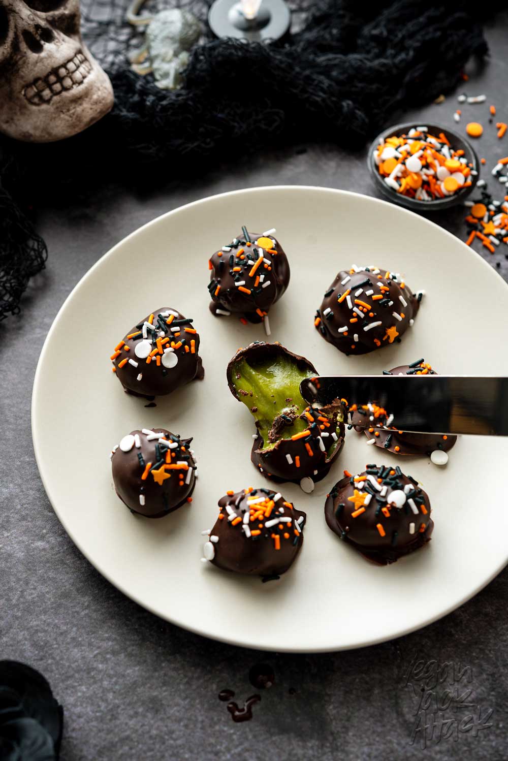 Small light grey plate of truffles with green filling on a black marble background