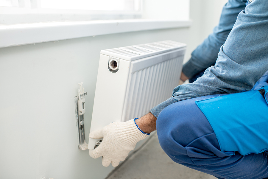 Workman mounting water heating radiator on the white wall indoors, close-up view
