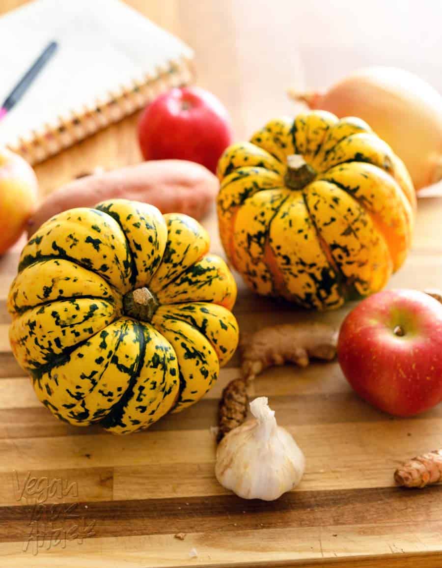 two acorn squash on a cutting board with apples, turmeric, ginger, and garlic