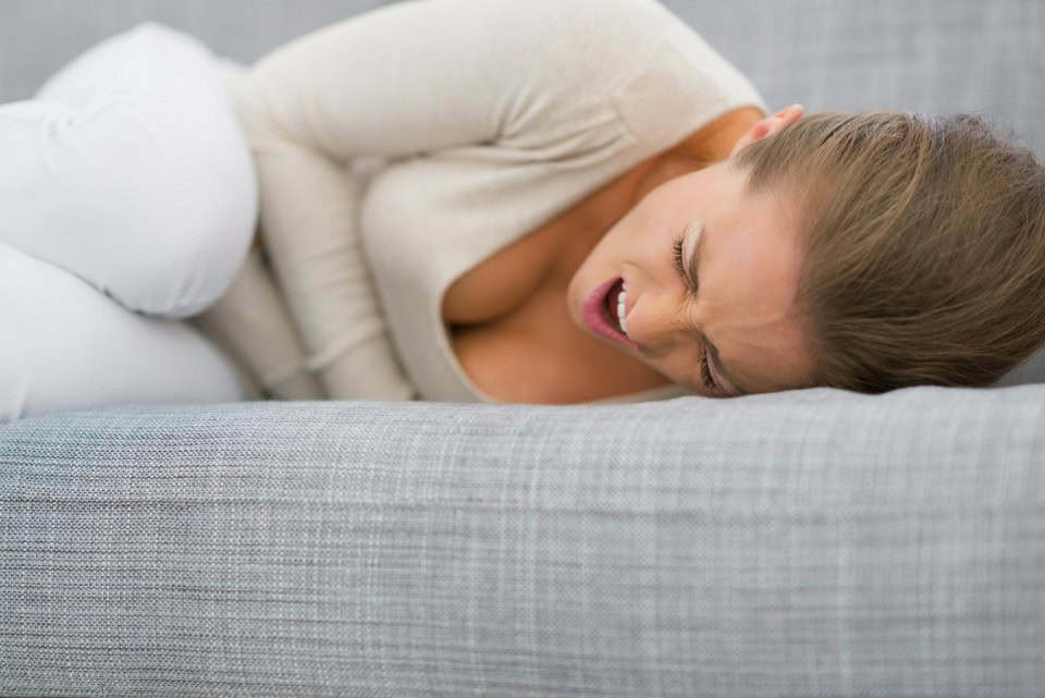 Young woman with stomach ache laying on sofa | Dicas de Saúde