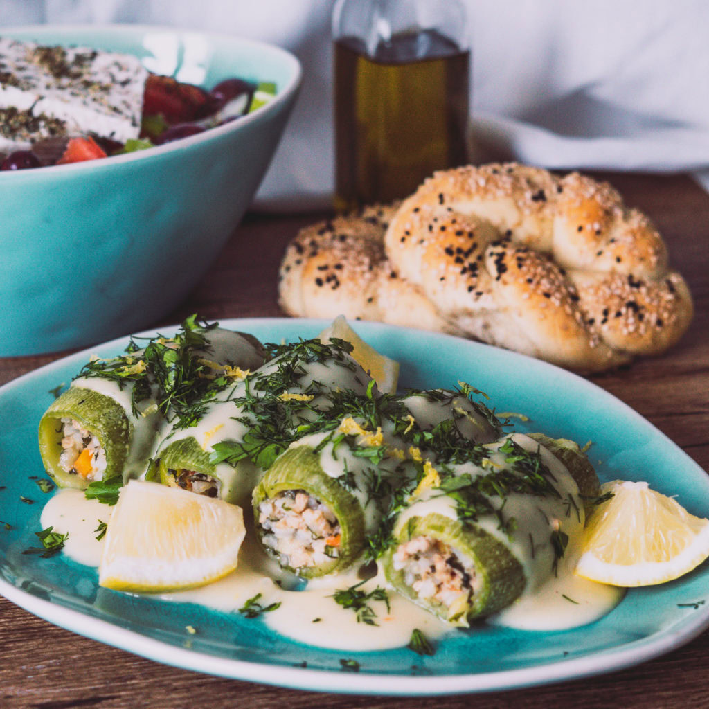 Gefüllte Zucchini mit Zitrone auf einem türkisen Teller, Sesamringe und Salat im Hintergrund