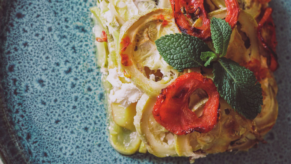 ein Stück griechischer Zucchiniauflauf mit Tomaten und Minze auf einem blauen Teller