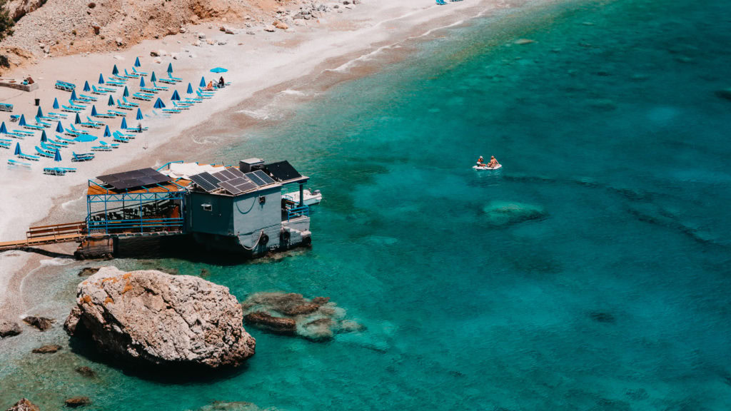 Ein Bild vom Strand von Glyka Nera mit einer Taverne, die auf dem Wasser schwimmt.
