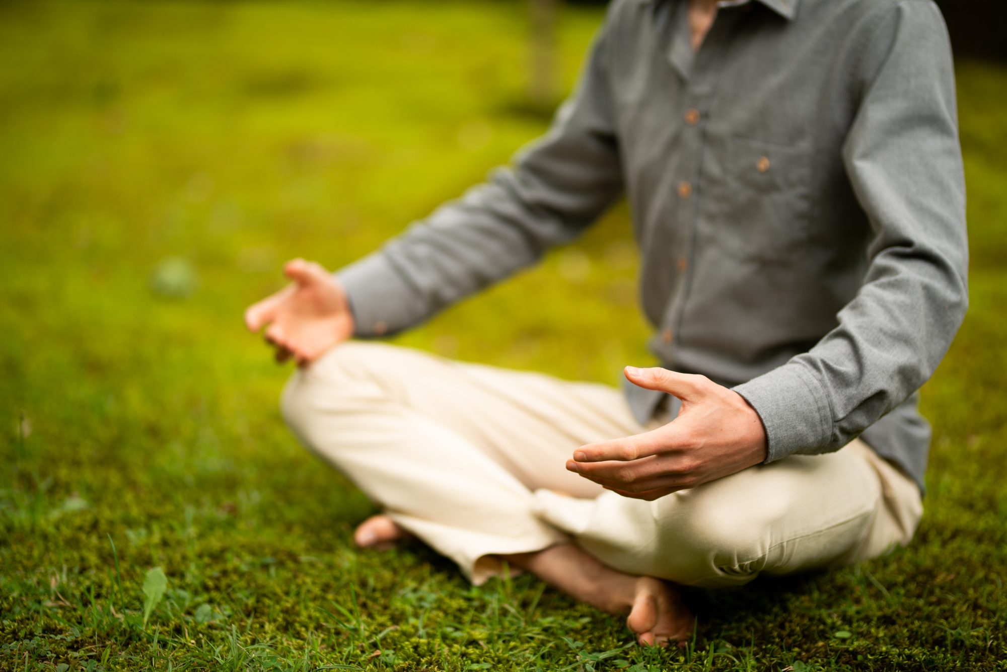 Mindfulness Individueel: Trainer zittend in meditatiehouding in het gras.