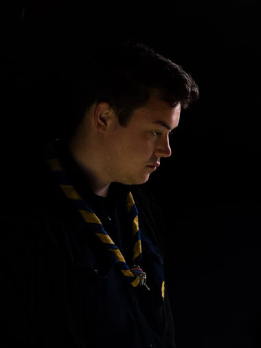 Portrait eines Pfadfinders vor dunklem Hintergrund. / Portrait of a boy scout against a dark background.
