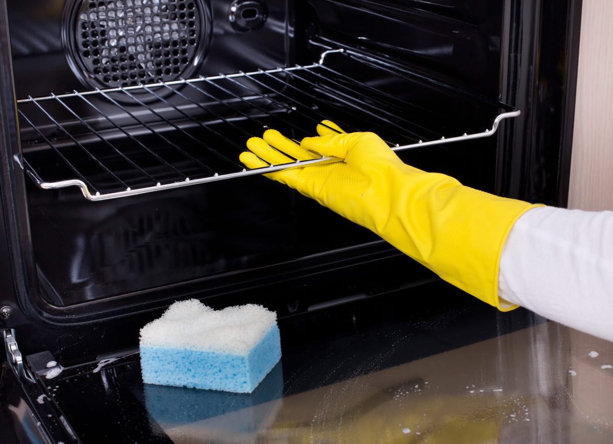Things you forget to clean-Close up of female hand with yellow protective gloves cleaning oven